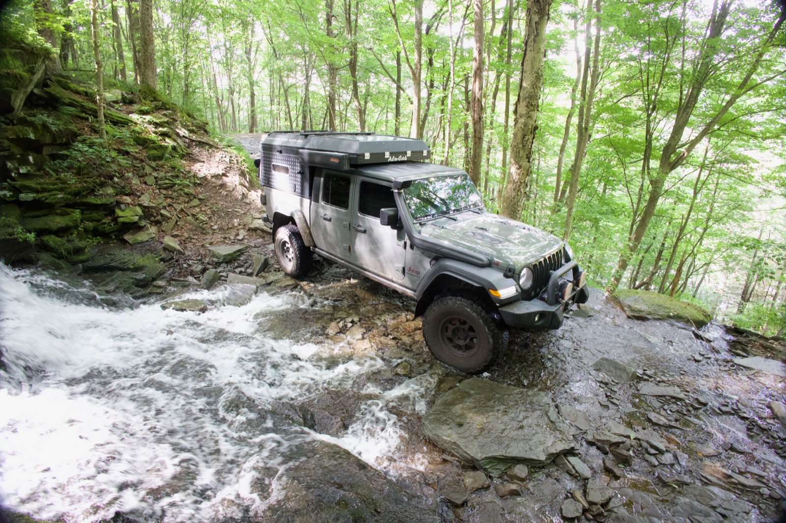 Jeep Gladiator crossing a rocky creek near a waterfall