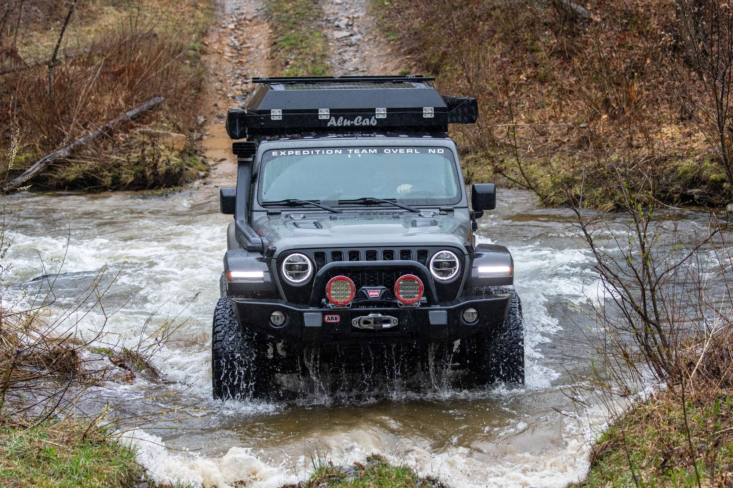 Lifted Jeep Wrangler with a roof-top rack crossing a rocky creek on the PA Wilds Pennsylvania BDR-X trail