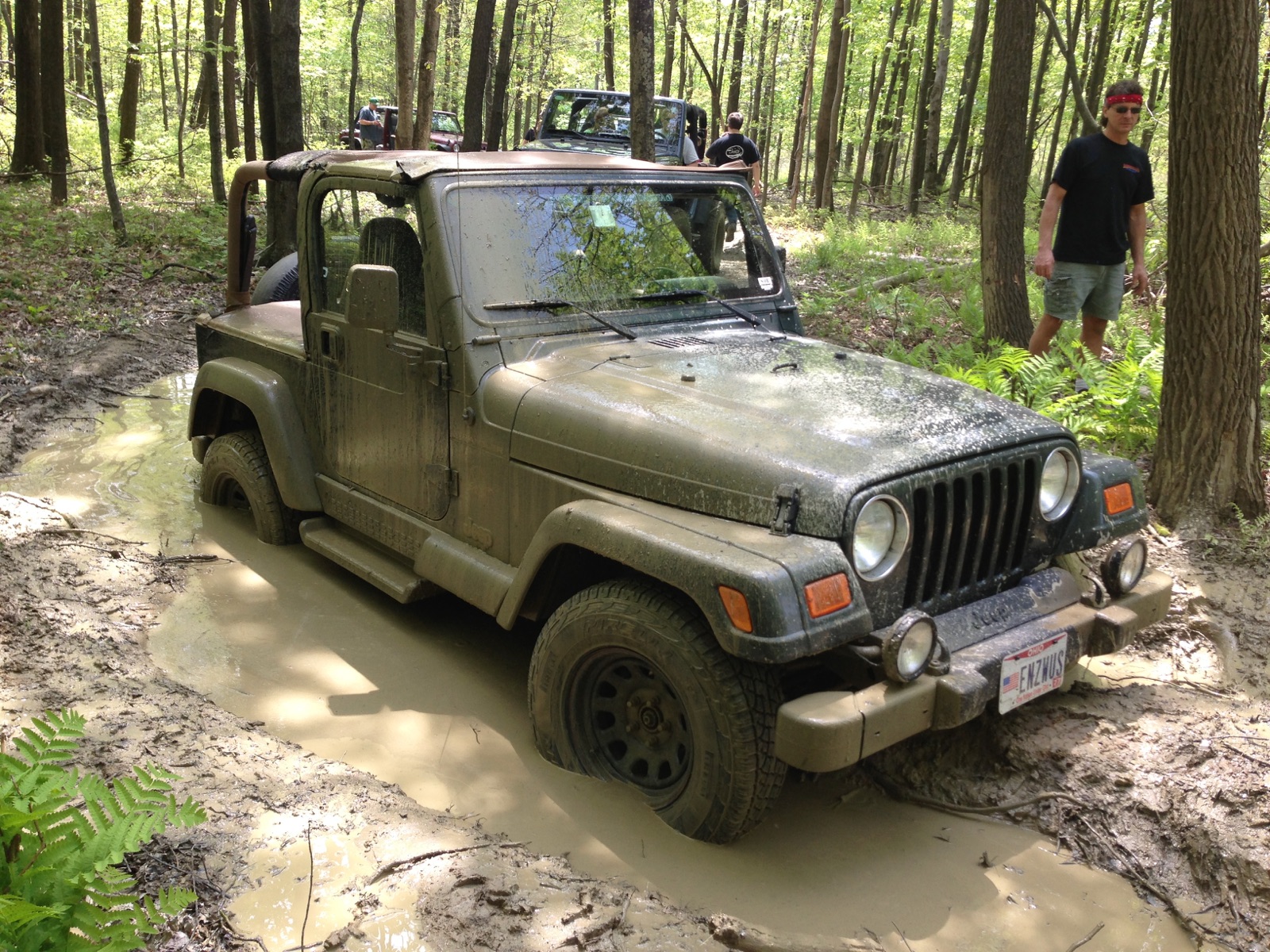 Mud-covered 2002 Jeep Wrangler Sahara negotiating a forest trail
