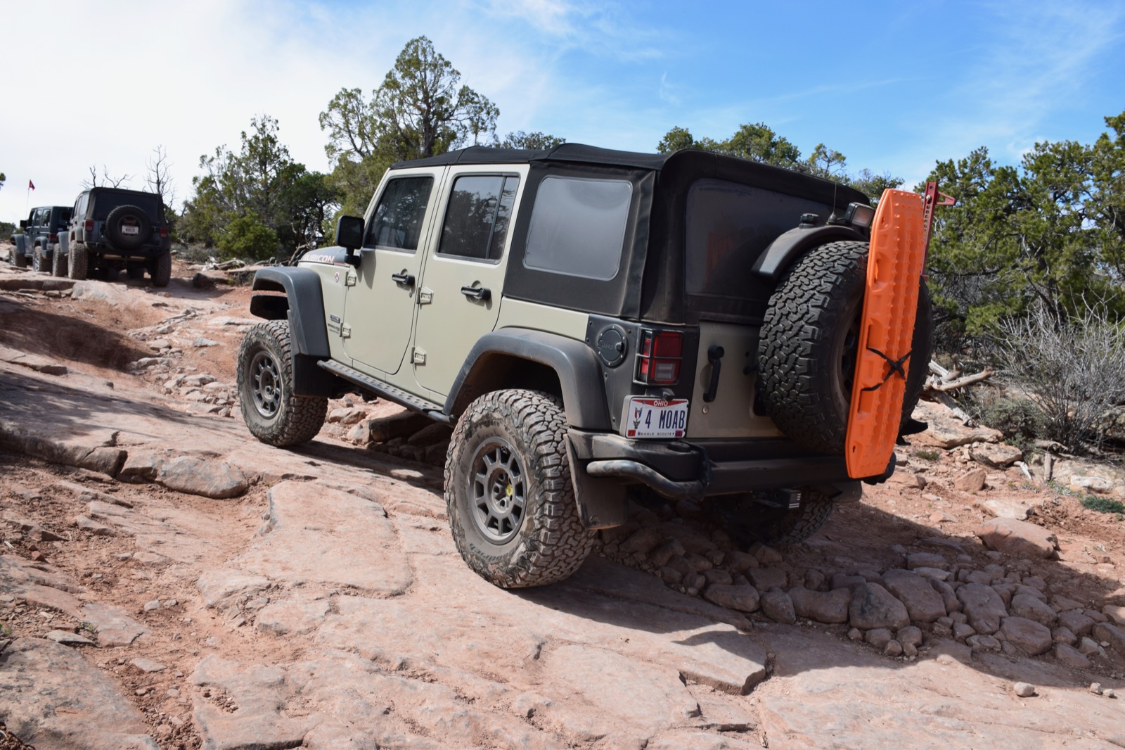 Wrangler climbing a stepped red-rock trail with a trail spotter